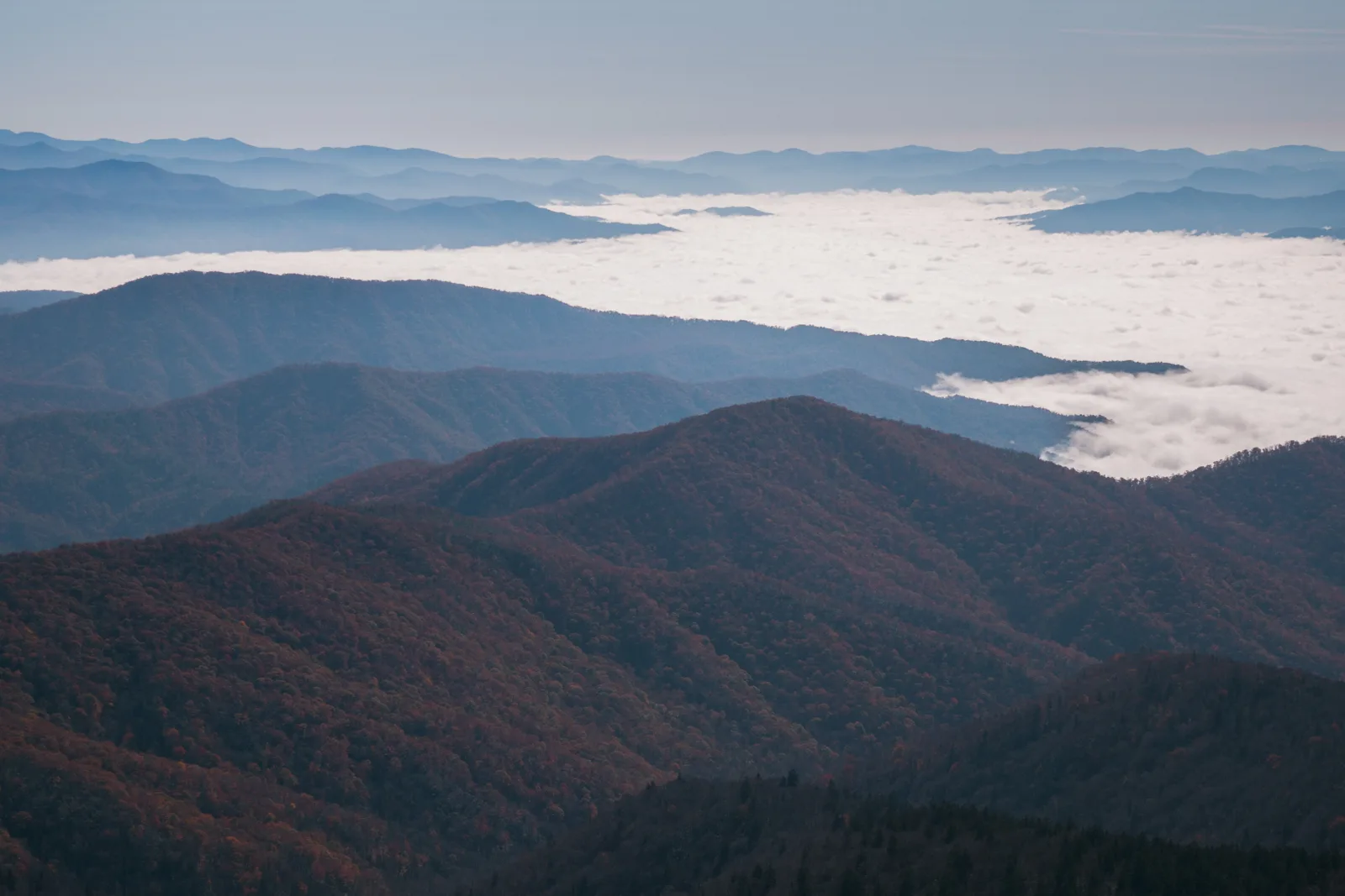Layered blue mountain ridges rising above a valley filled with low cloud.