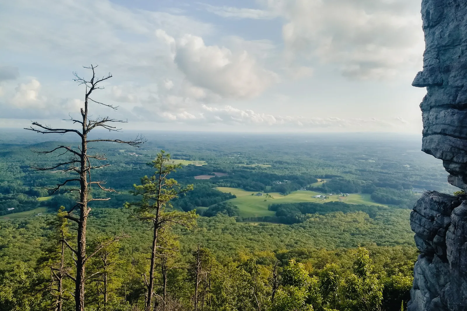 The view from a rocky outcrop over forested hills and distant farmland.