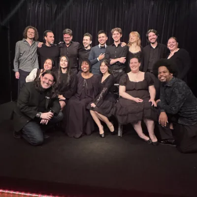 A theatre cast of about sixteen, dressed in black, posed together on stage after a Shakespeare performance.